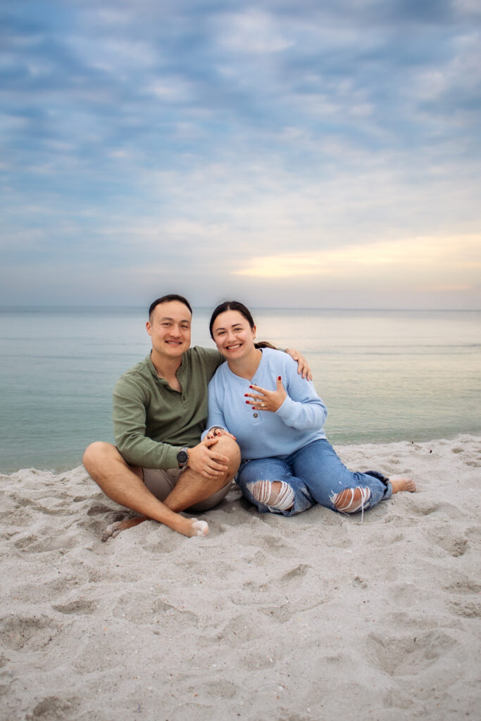 Couple engagement photos on a beach of couple showing off the ring