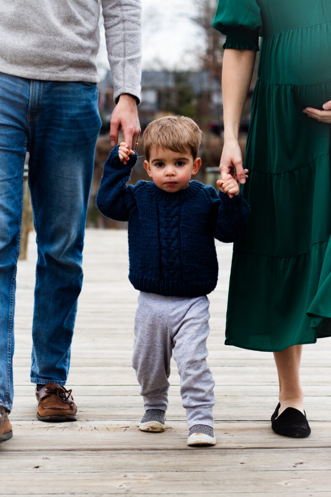 Family maternity portrait of toddler standing between mom and dad.