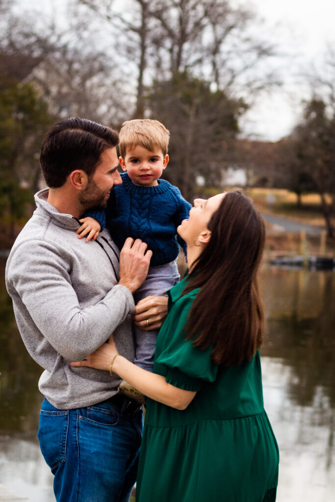 Family portrait of mom and dad laughing and looking at toddler.