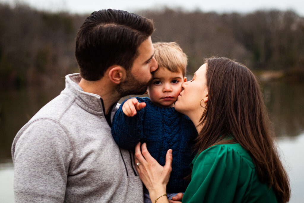 Family portrait taken on dock in Edgewater, MD where mom and dad are kissing the toddler's cheeks.